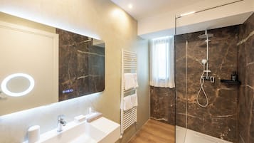 A modern bathroom with a marble wall, a glass-enclosed shower, a white sink, and a towel rack.