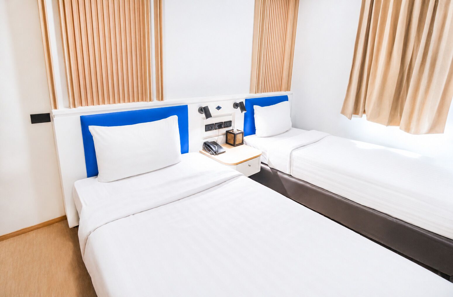 A hotel room with two beds, a bedside table with a lamp, and a phone.
