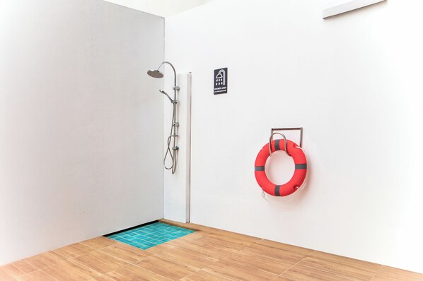 A shower area with a showerhead, a sign indicating the shower area, and a life preserver on the wall. - Citin Armoni Patong Hotel by Compass Hospitality (Patong)