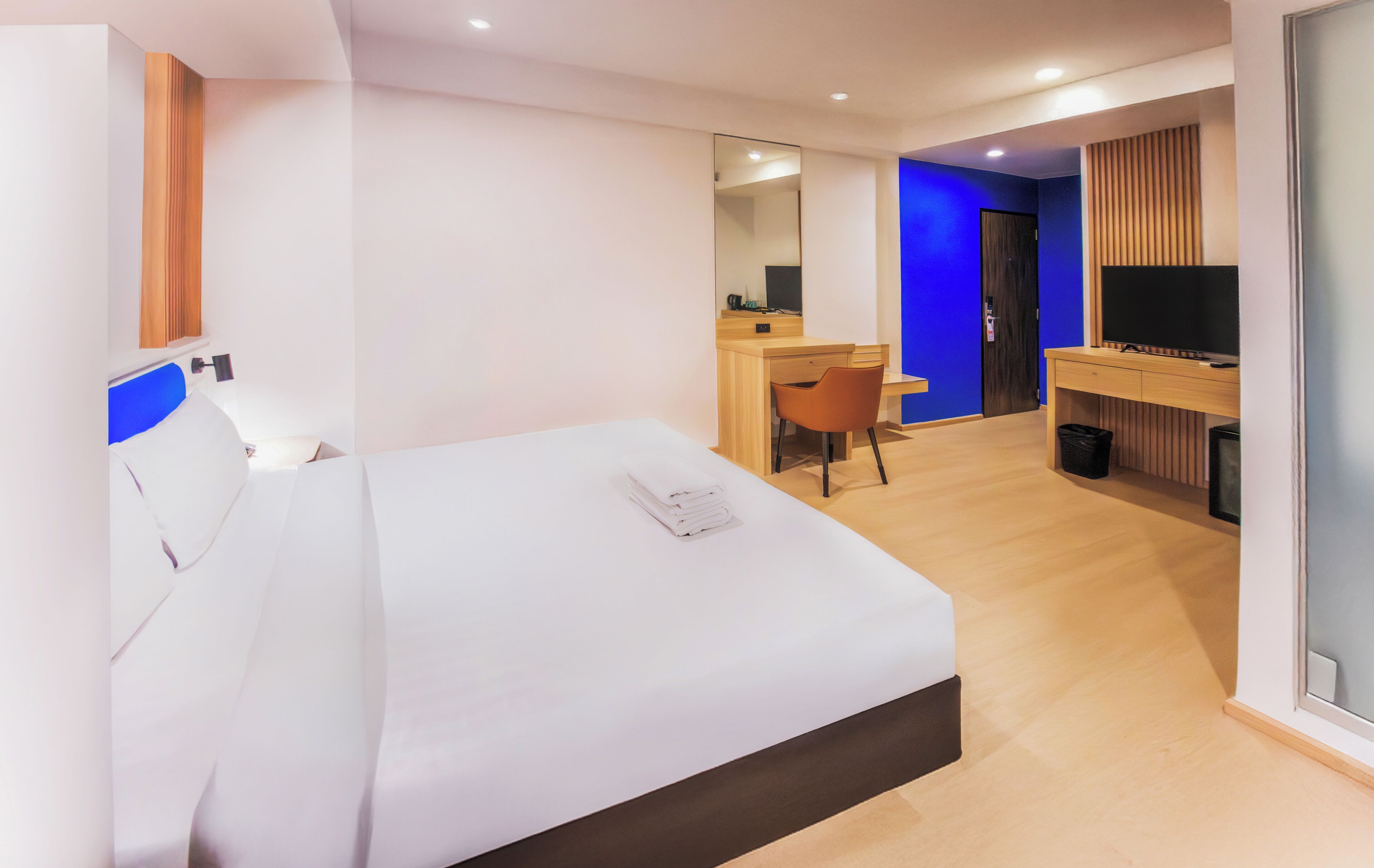 A hotel room with a bed, a desk, a chair, a television, and a mirror.