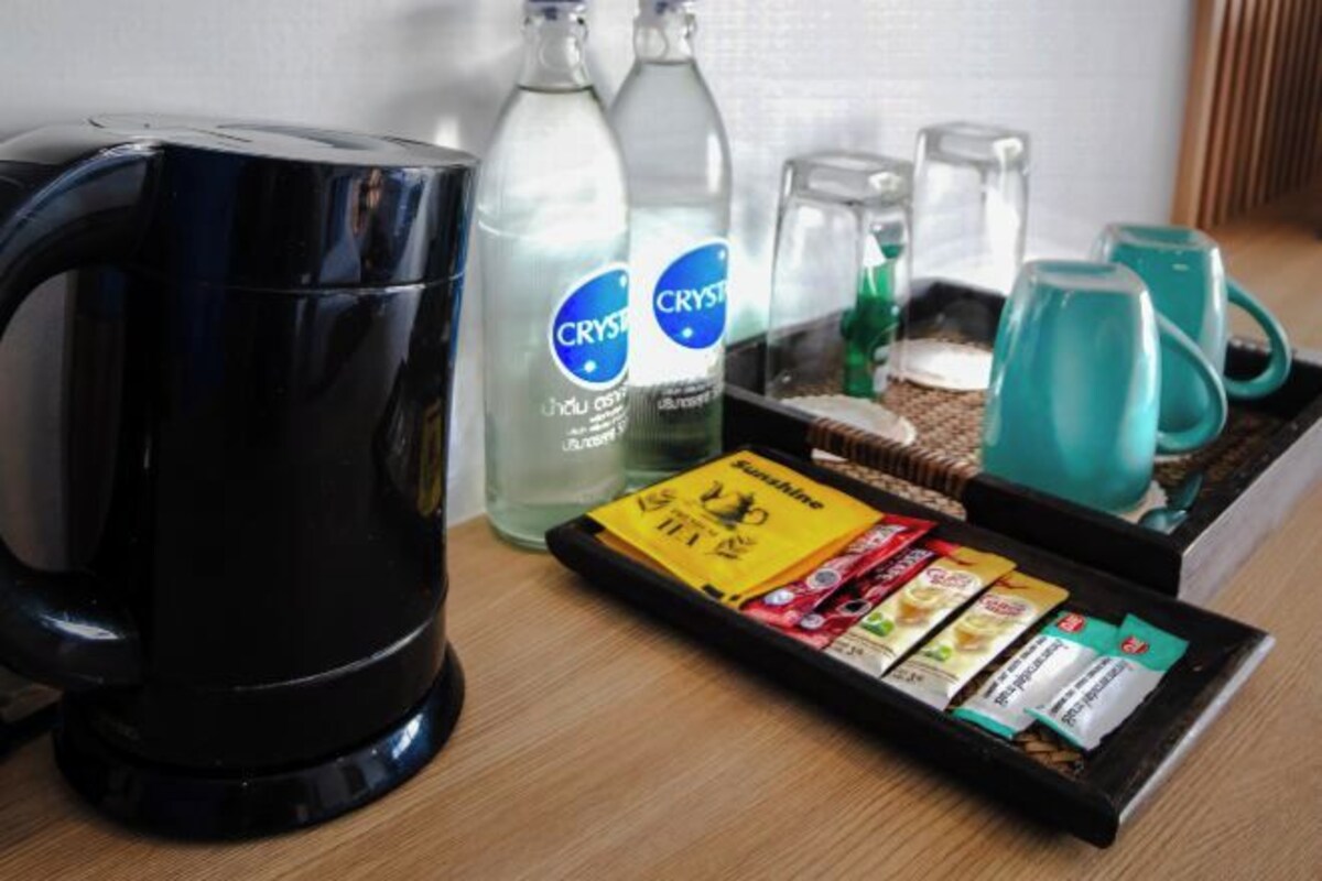 A coffee maker, two bottles of Crystal Geyser water, a tray with tea bags, and teal mugs on a wooden table.