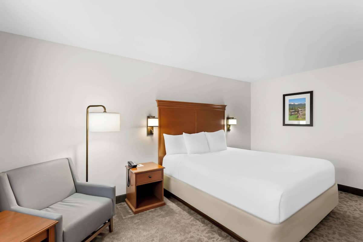 A hotel room with a bed, a nightstand, a lamp, a chair, and a small table.