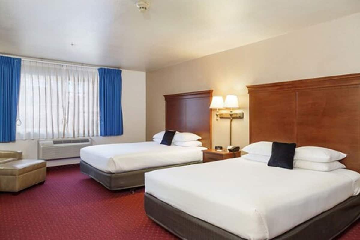 A hotel room with two beds, a desk, a chair, a lamp, and a window with curtains.