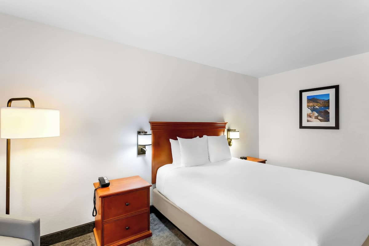 A hotel room with a large bed, a bedside table with a lamp, a phone, and a small desk.