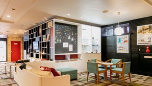 A modern lobby with a white sofa, teal chairs, a patterned carpet, and a blackboard with various notes and drawings. - KOKO STAY Chitose (Chitose)