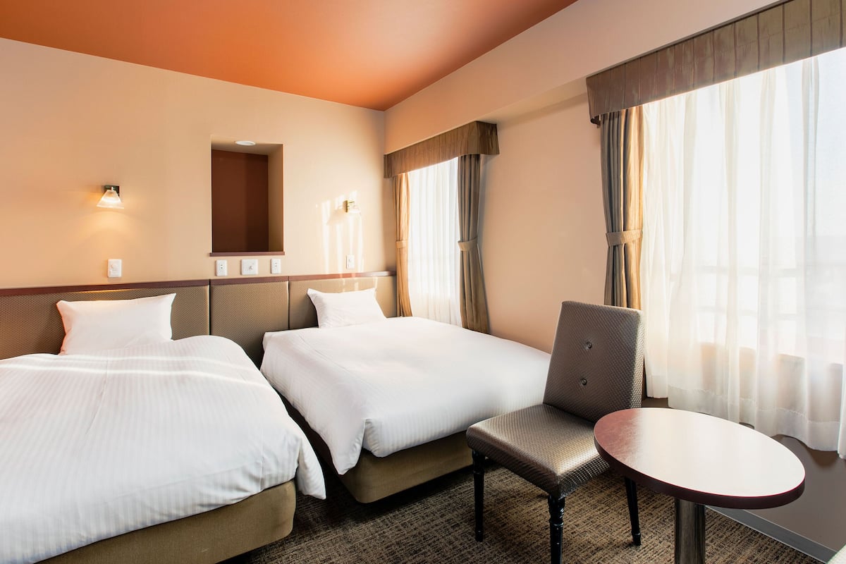 A hotel room with two beds, a chair, a small table, and a mirror.
