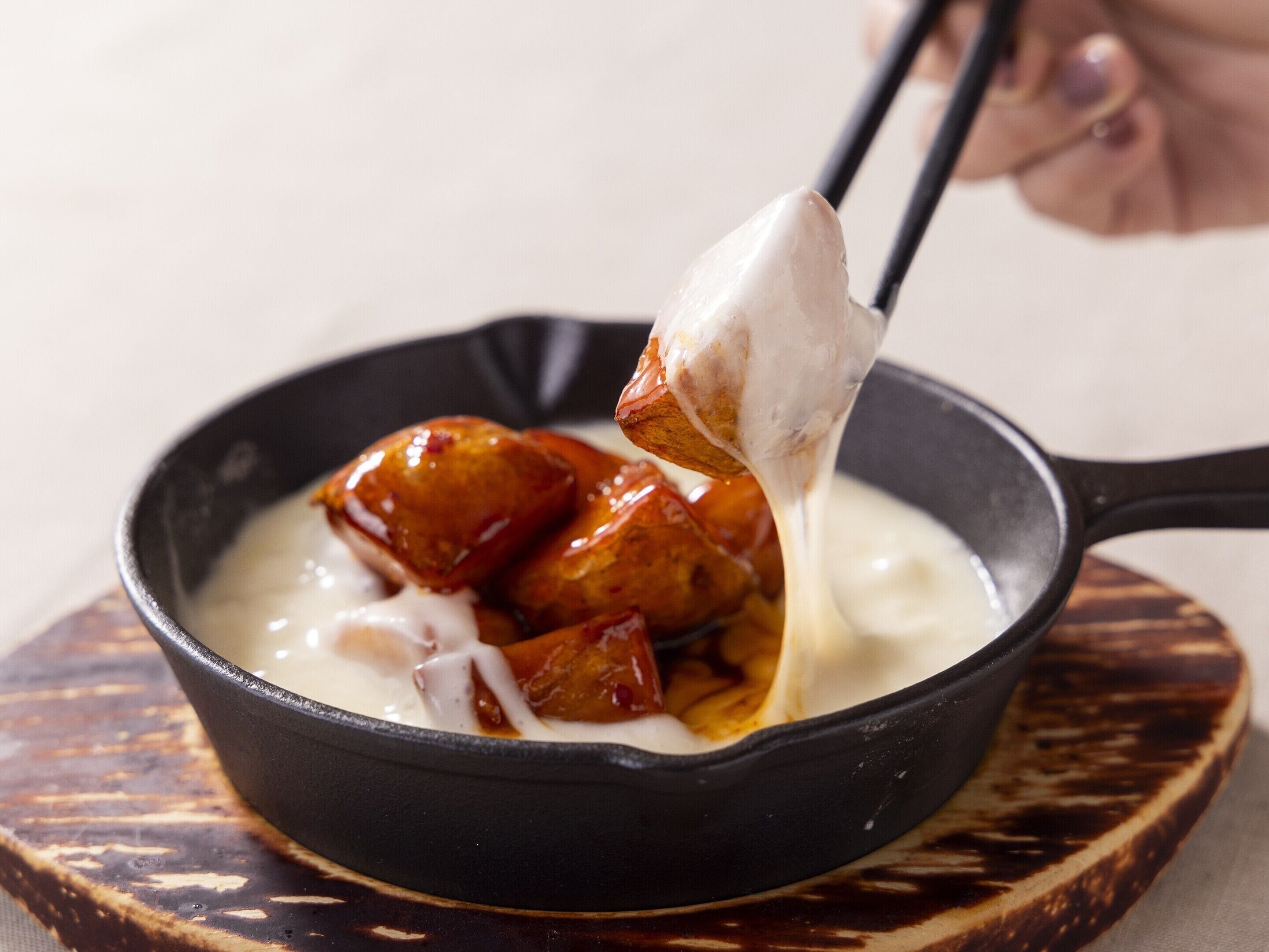 A bowl of food with a spoon lifting a piece, placed on a wooden board.