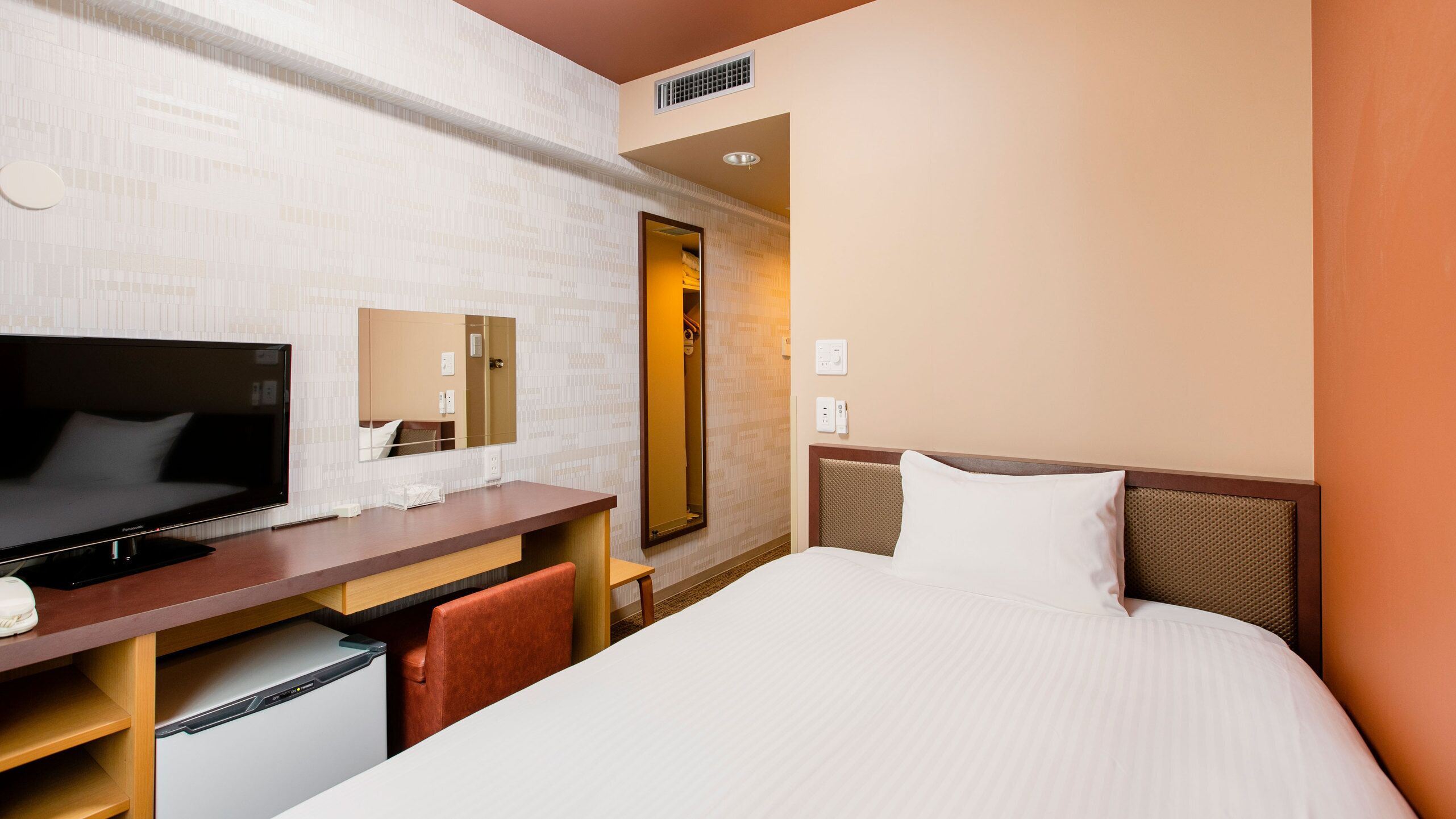 A hotel room with a bed, a TV, a desk, a mirror, and a wardrobe.