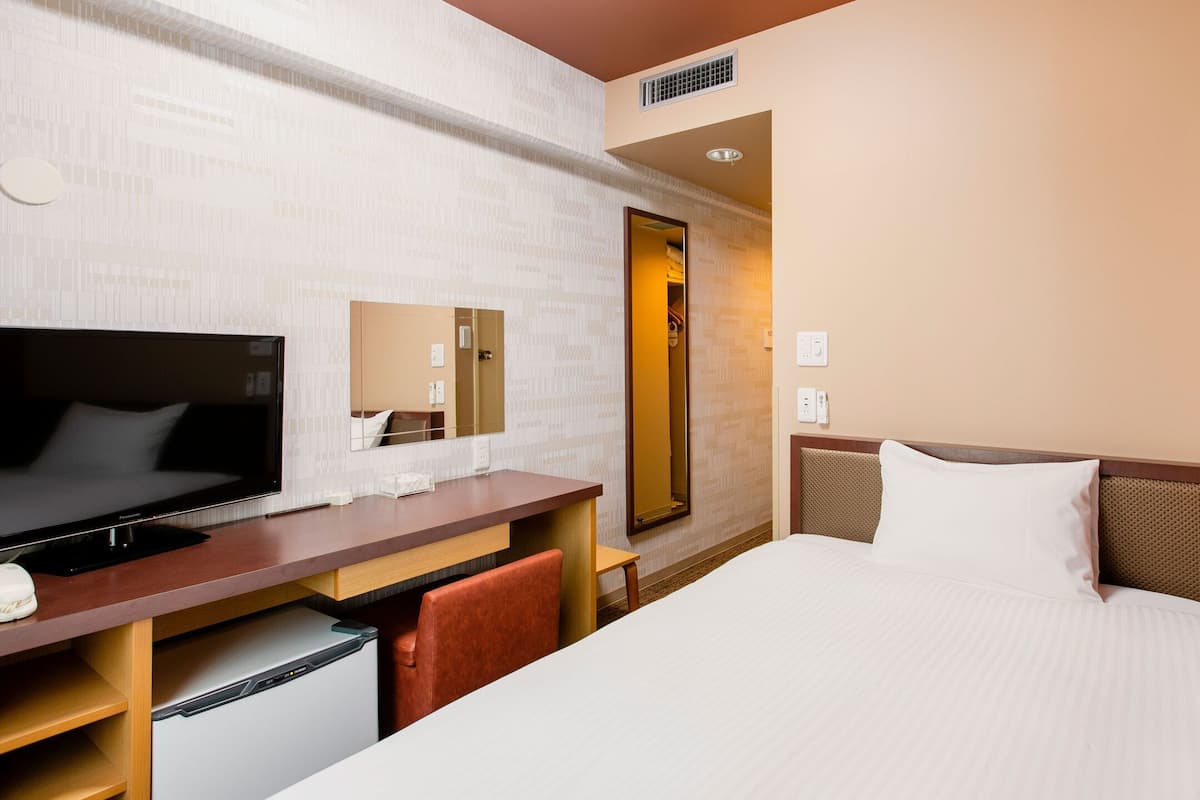 A hotel room with a bed, a TV, a desk, a mirror, and a wardrobe.