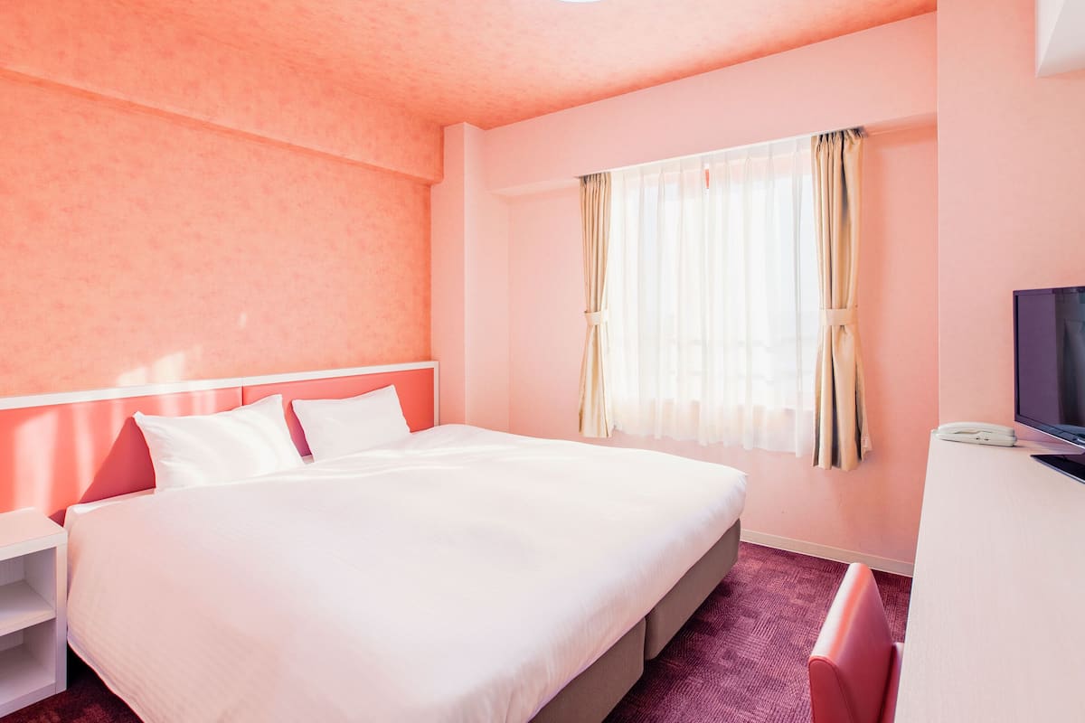 A hotel room with a large bed, a desk with a computer, and a window with curtains.