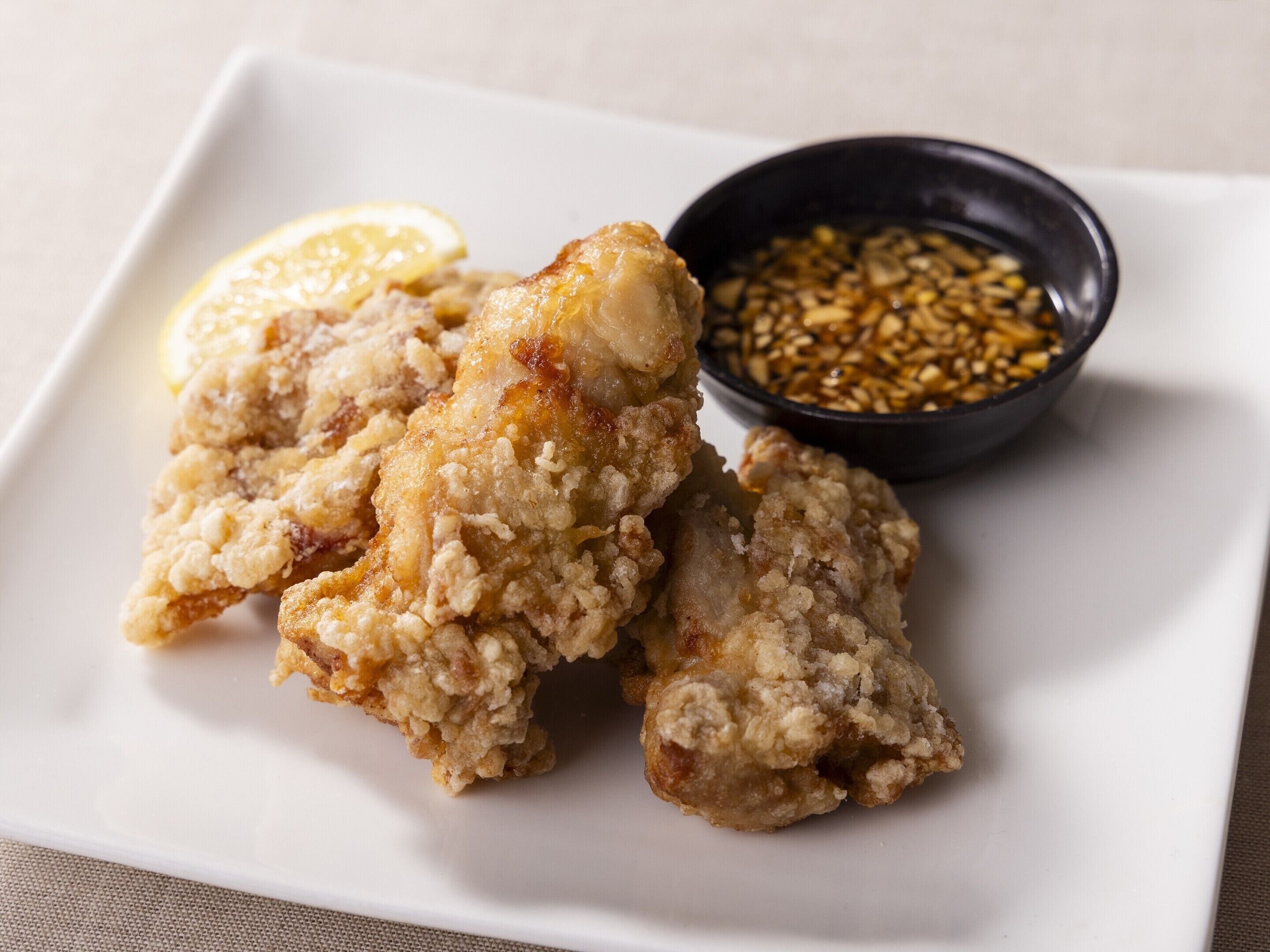 A plate of fried chicken with a lemon wedge and a bowl of sauce.