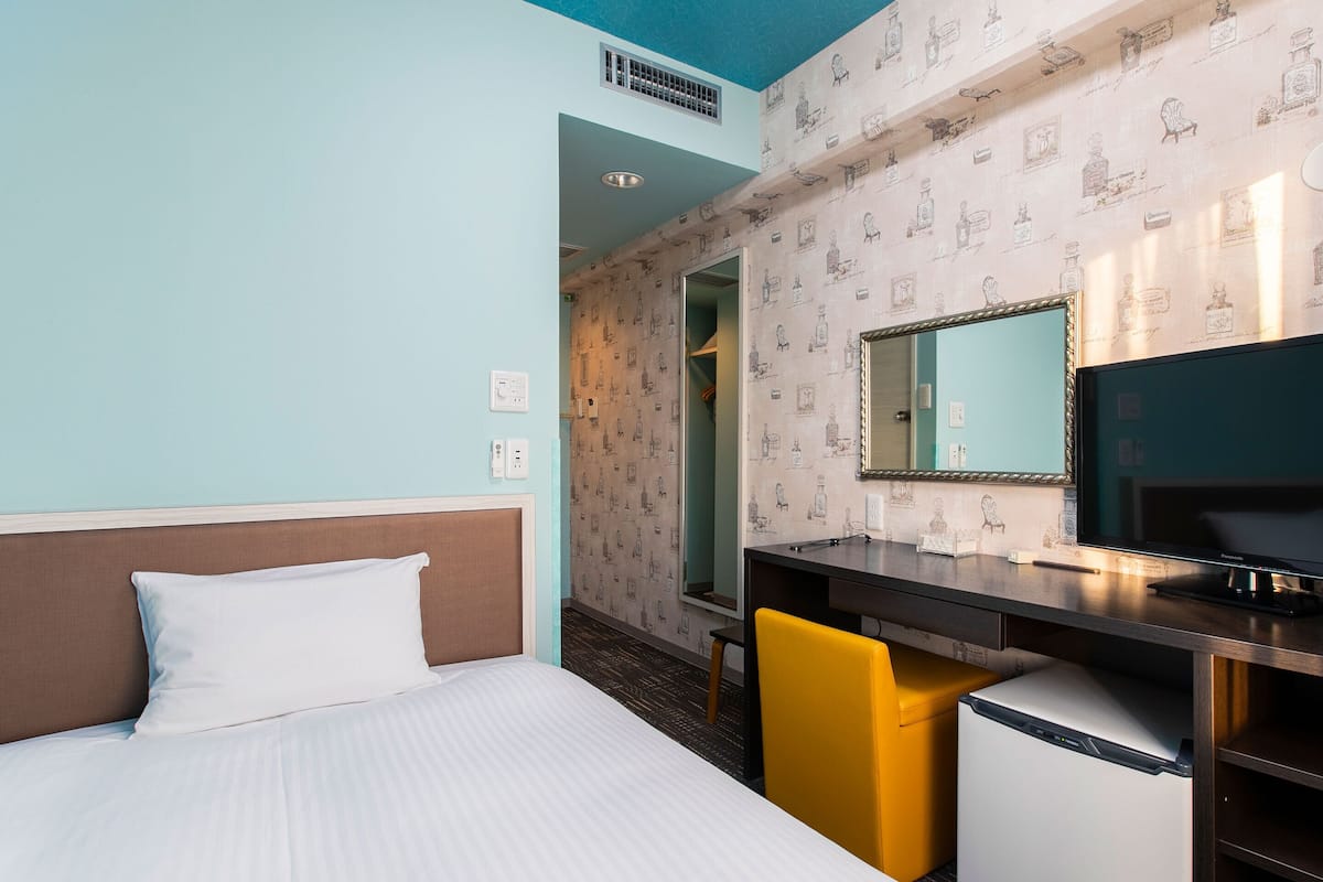 A hotel room with a bed, a desk with a computer, a chair, a television, and a mirror.