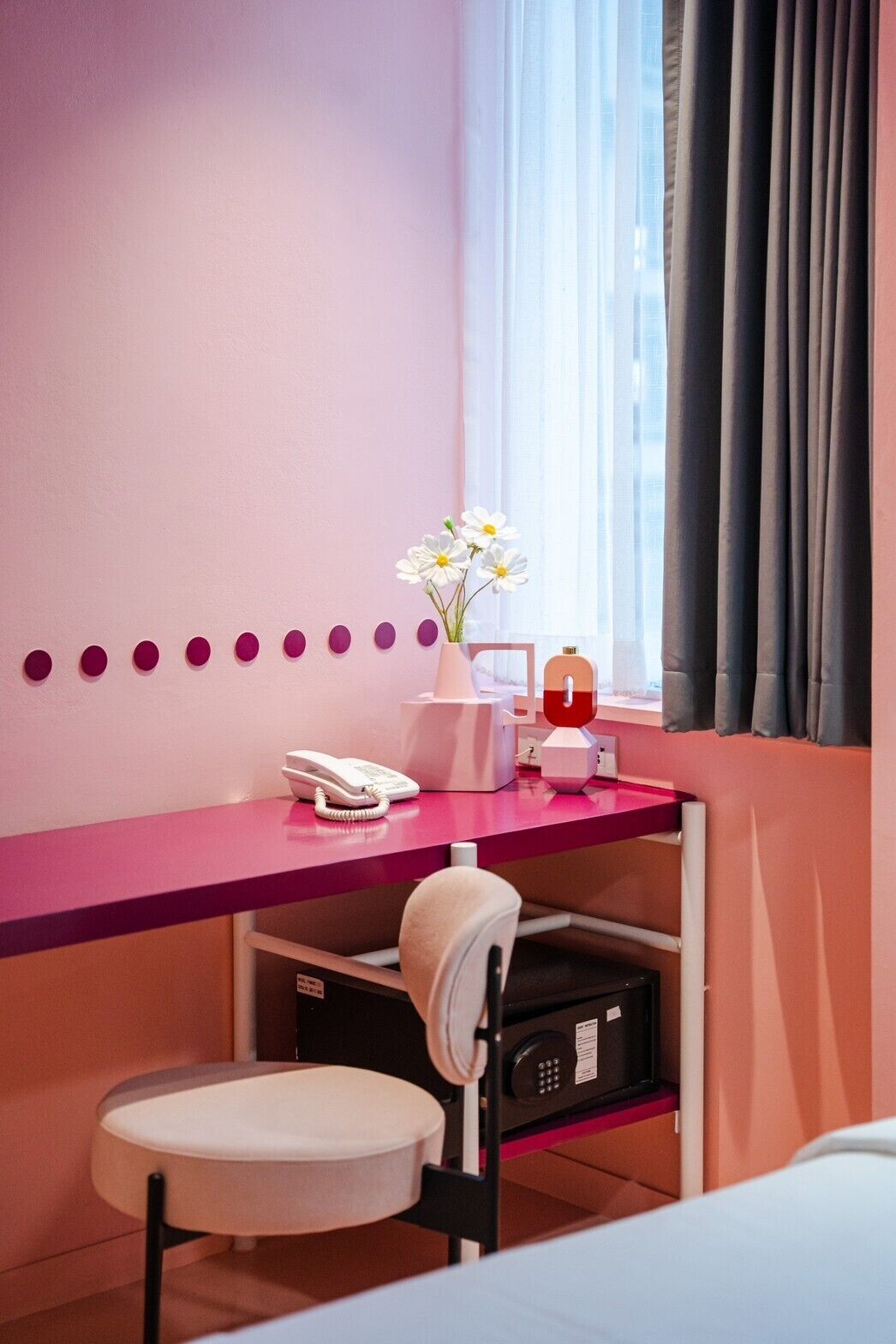 A pink desk with a phone, a vase with flowers, and a small shelf with a bottle.