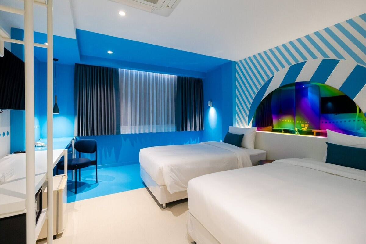 A modern hotel room with two beds, a desk, and a chair.
