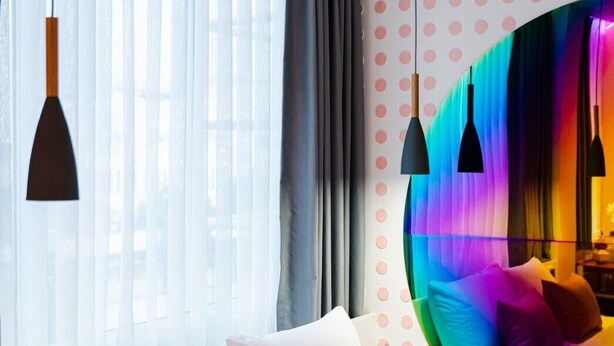 A modern bedroom with a bed, pillows, a window with curtains, and a colorful wall feature. - Budacco (Bangkok)
