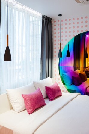A modern bedroom with a bed, pillows, a window with curtains, and a colorful wall feature. - Budacco (Bangkok)