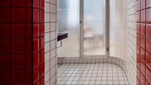 A bathroom with red and white tiled walls, a frosted glass shower door, and a white tiled floor. - Budacco (Bangkok)