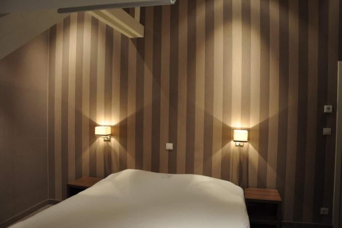 Una habitación de hotel con papel tapiz a rayas, dos lámparas de noche y una cama bien hecha.