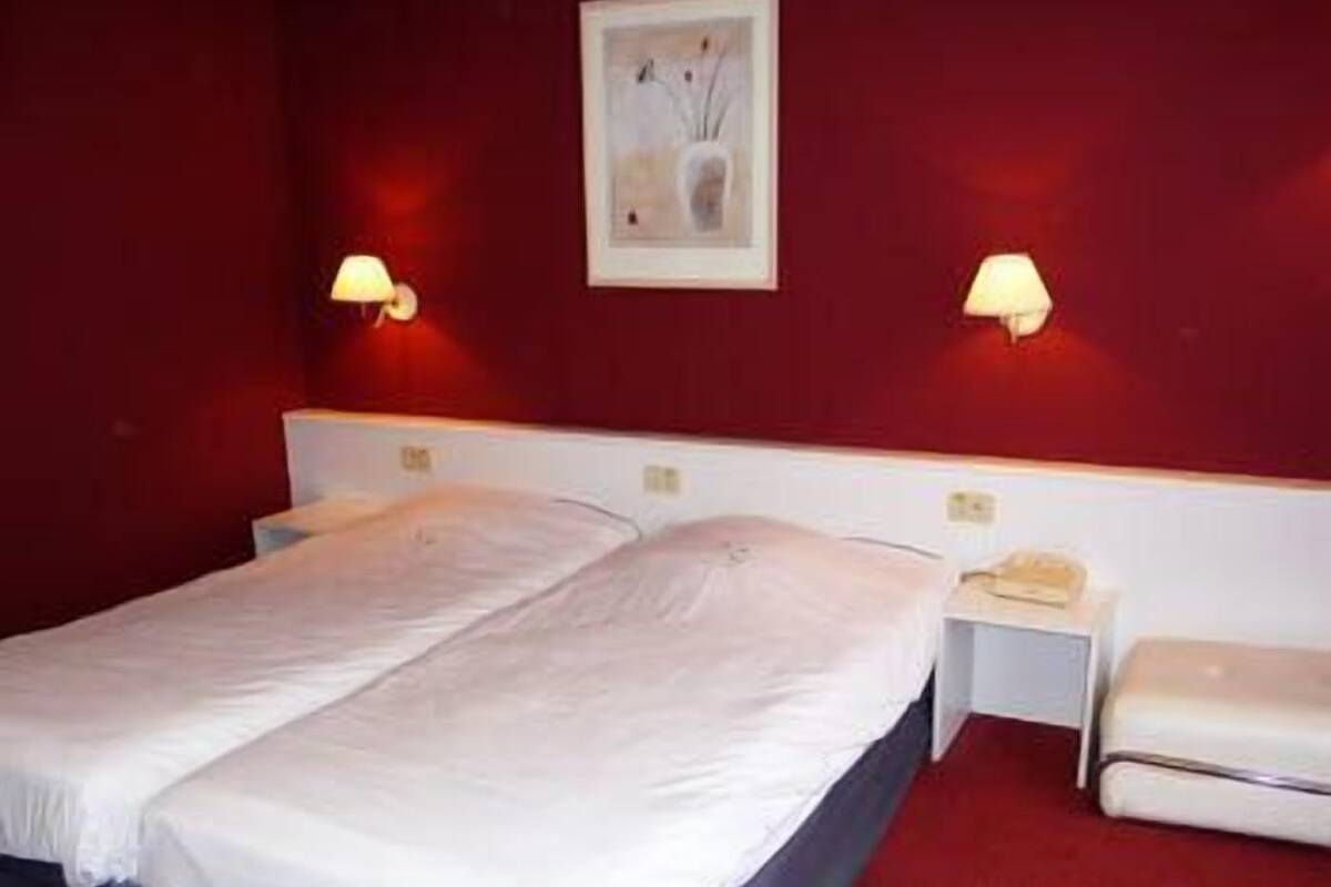 Una habitación de hotel con una cama grande, dos mesitas de noche y una mesita de noche con lámpara.