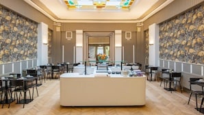 Un hall d’hôtel doté d’un comptoir d’accueil central, d’un papier peint à motifs et d’un plafond en vitraux.