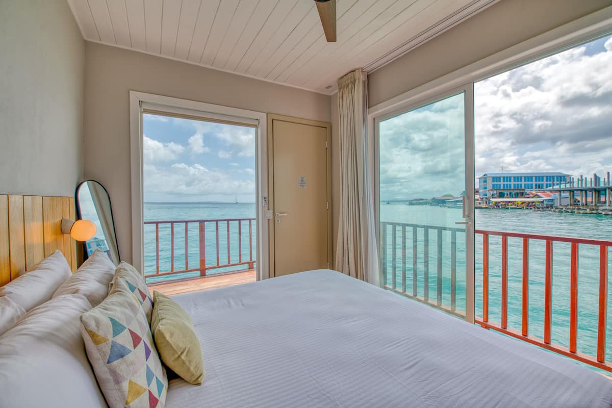 A hotel room with a large bed, a view of the sea, and a balcony with a railing.