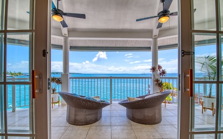 A covered balcony with two wicker chairs, a view of the sea, and ceiling fans.
