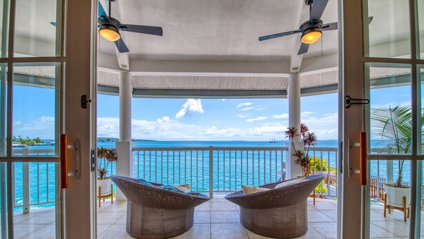 A covered balcony with two wicker chairs, a view of the sea, and ceiling fans. - Tropical Suites Hotel (Bocas del Toro)