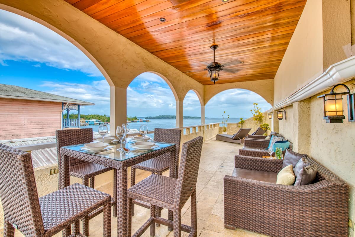 An outdoor patio with wicker furniture, a ceiling fan, and a view of the sea.