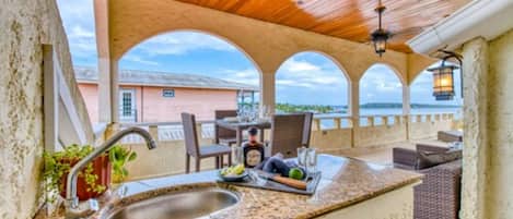 A covered outdoor kitchen area with a sink, bar tools, and seating.