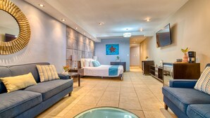 A modern living room with a sofa, a glass coffee table, a bed with a starfish artwork, and a TV mounted on the wall. - Tropical Suites Hotel (Bocas del Toro)