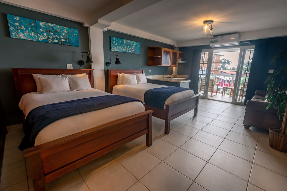 A hotel room with two wooden beds, a kitchenette, and a balcony with a view.