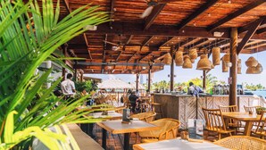 An outdoor restaurant with wooden tables and chairs, hanging wicker lamps, and a view of the ocean. - Tropical Suites Hotel (Bocas del Toro)
