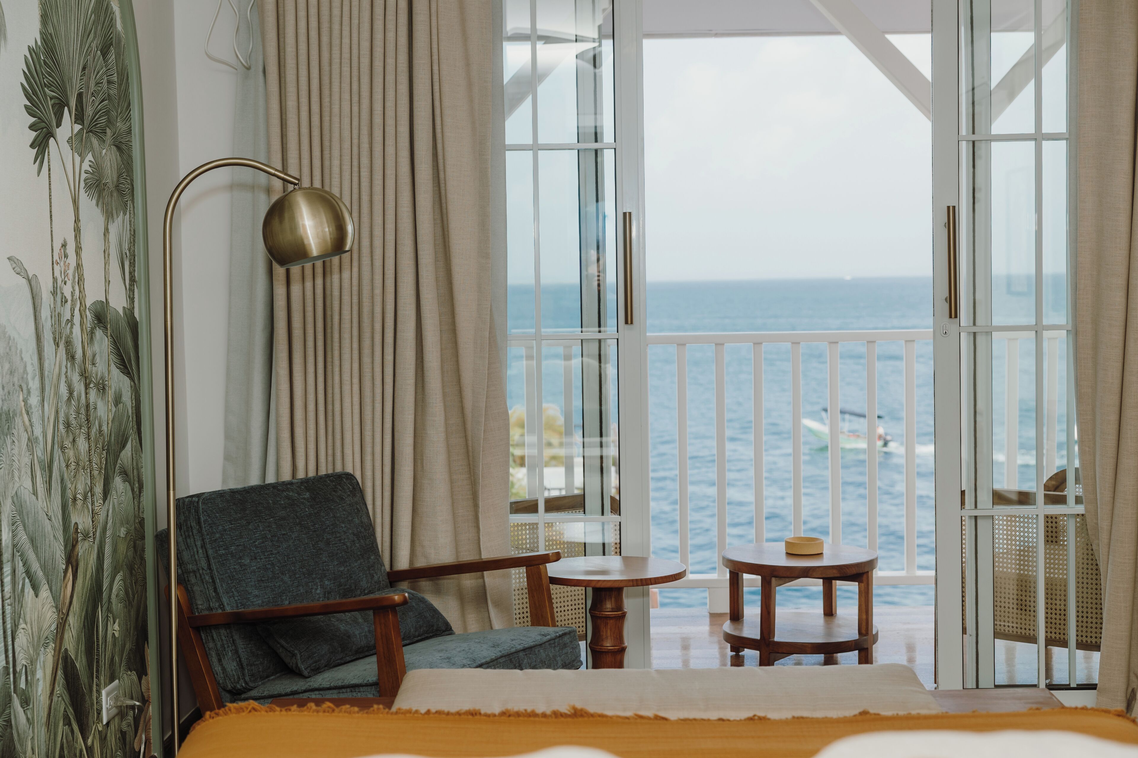 Une chambre avec un lit, une chaise, une petite table et une vue sur la mer, visible à travers de grandes portes vitrées.