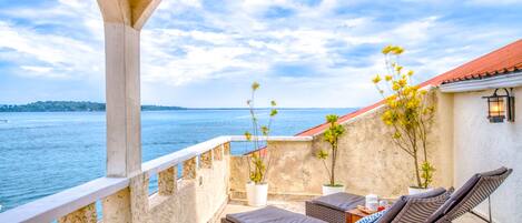 A balcony with wicker lounge chairs, potted plants, and a view of the sea.