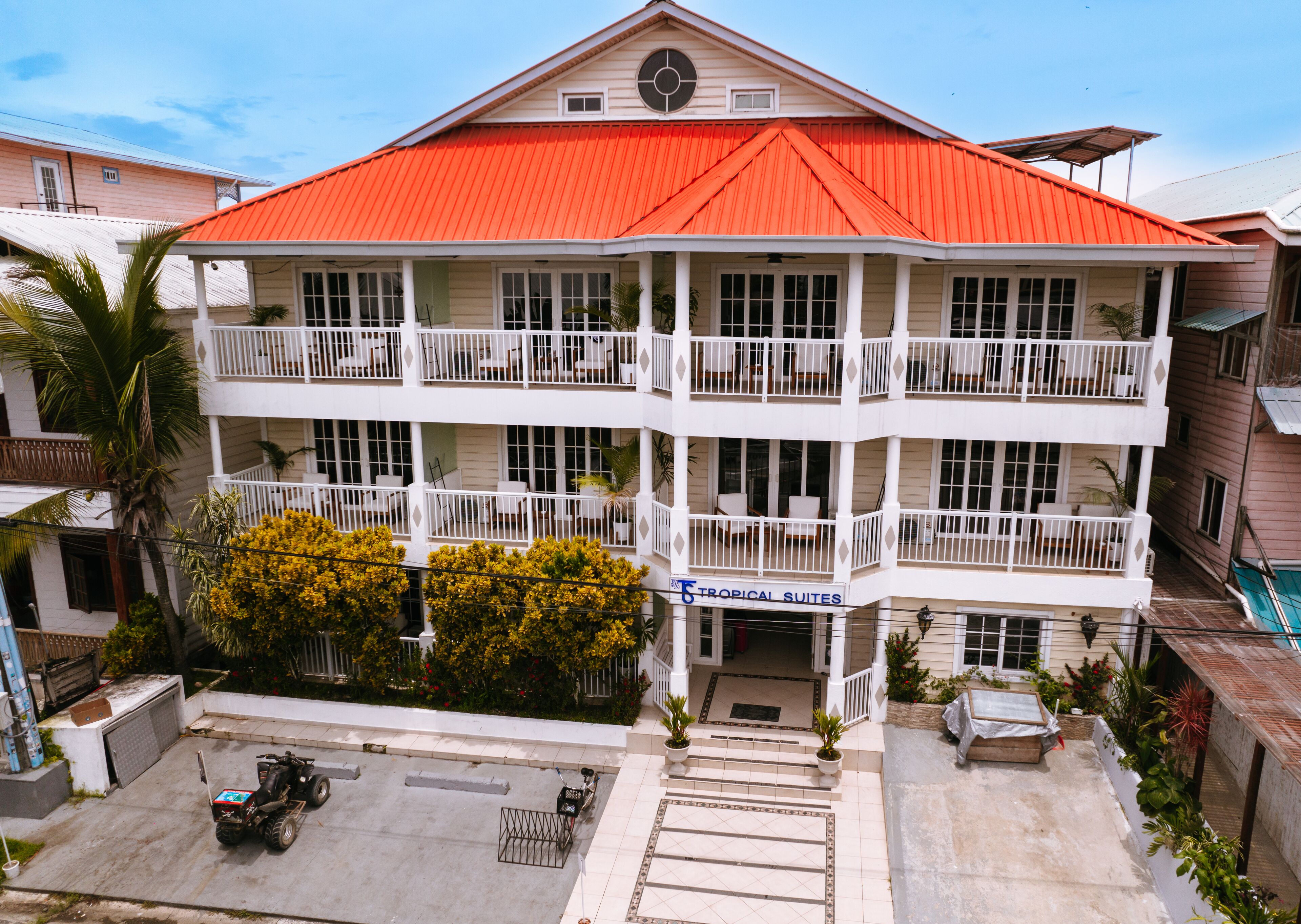 A multi-story hotel with a red roof, balconies, and a sign for 'Tropical Suites'.