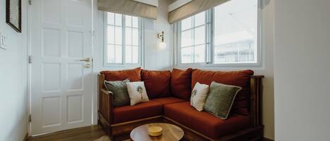 A room with a wooden floor, a brown sectional sofa, a round wooden coffee table, and a white door.