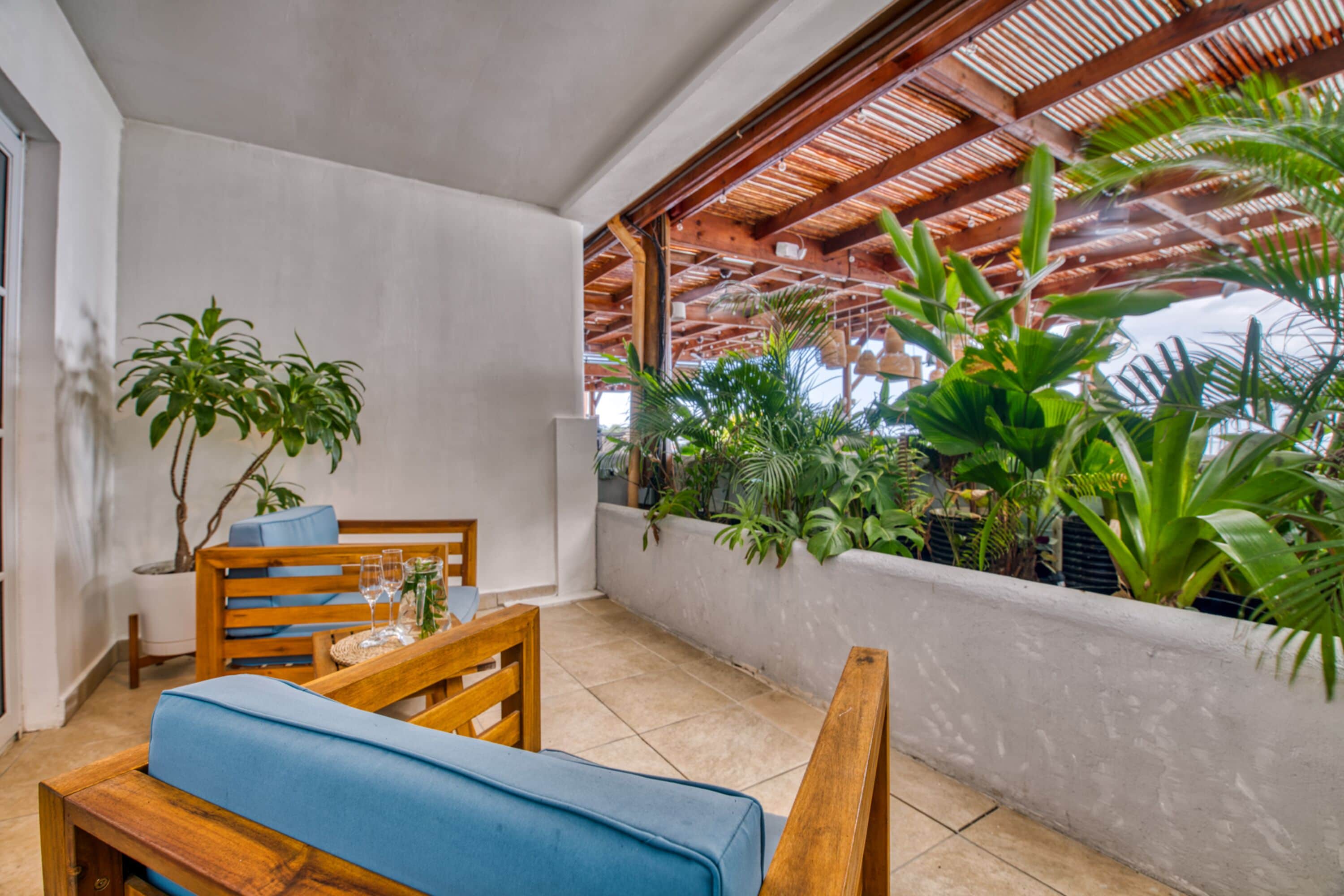 Uma varanda com um banco de madeira, um vaso com planta e vista para o verde.