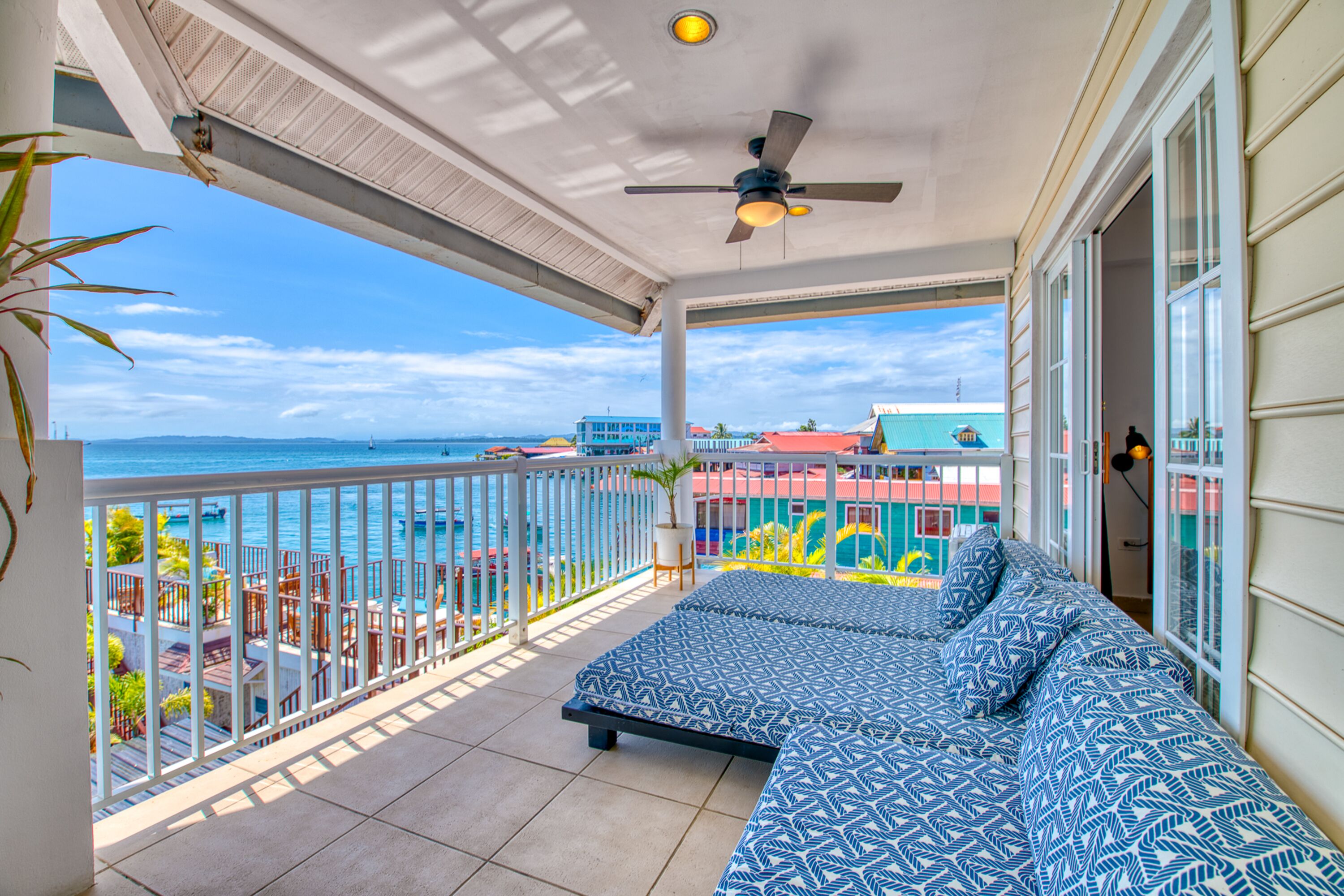 Een balkon met een bed, een plafondventilator en uitzicht op de oceaan.