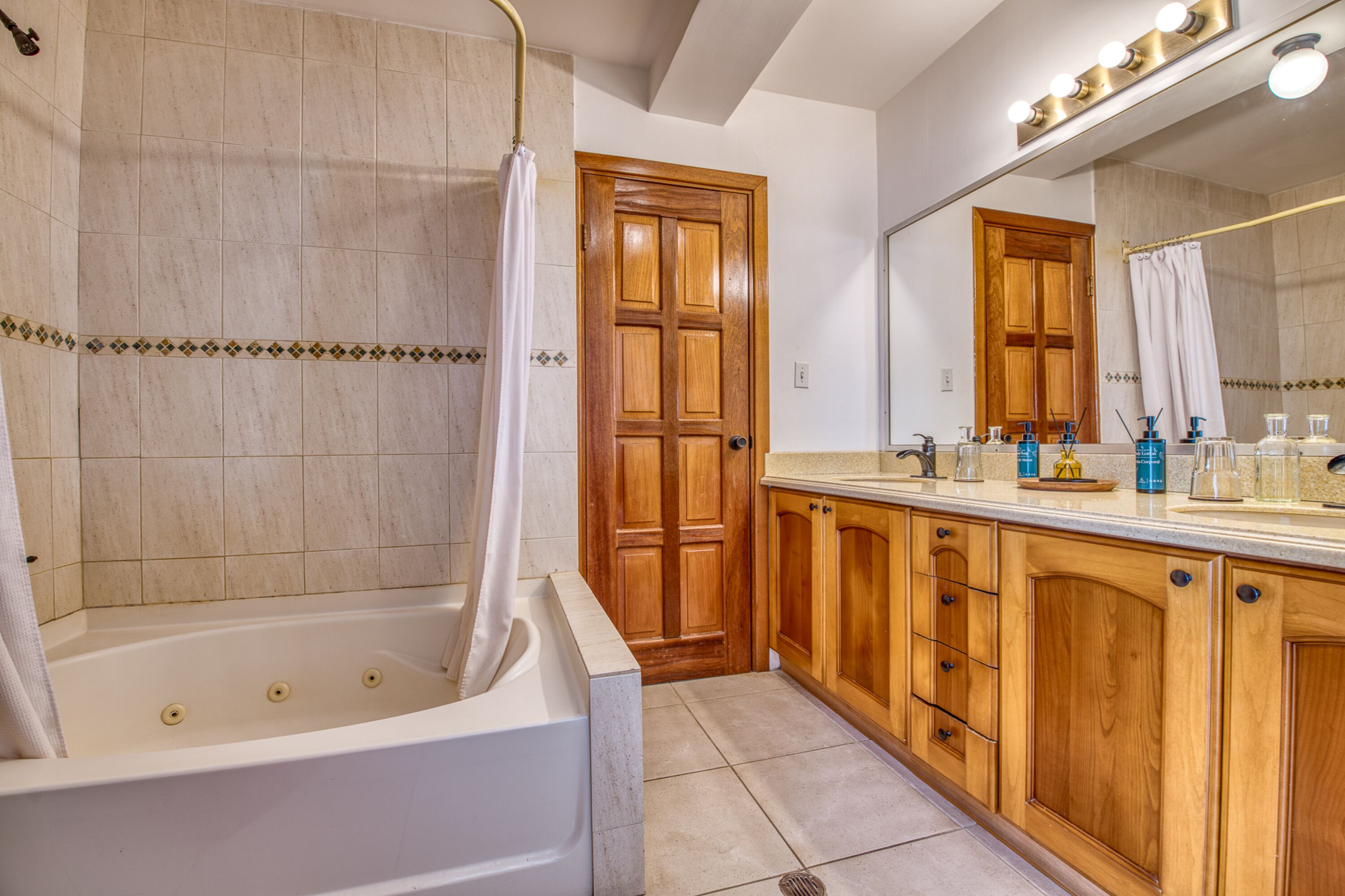 Ein Badezimmer mit Badewanne, Holzschränken, einem Waschtisch mit Spiegel und einer Duschvorhang.