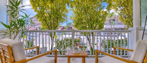 A balcony with two wooden chairs and a table, surrounded by white railings and green plants.