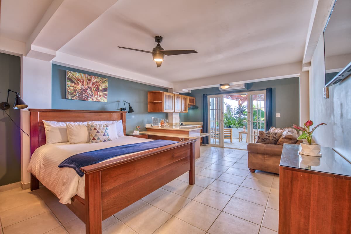 A spacious bedroom with a large bed, a desk, and a view to a balcony.