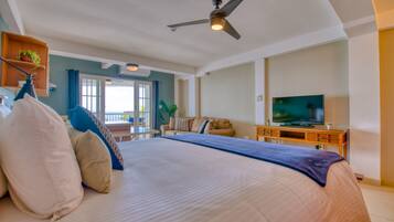 A spacious bedroom with a large bed, a ceiling fan, a television, and a balcony with a view.