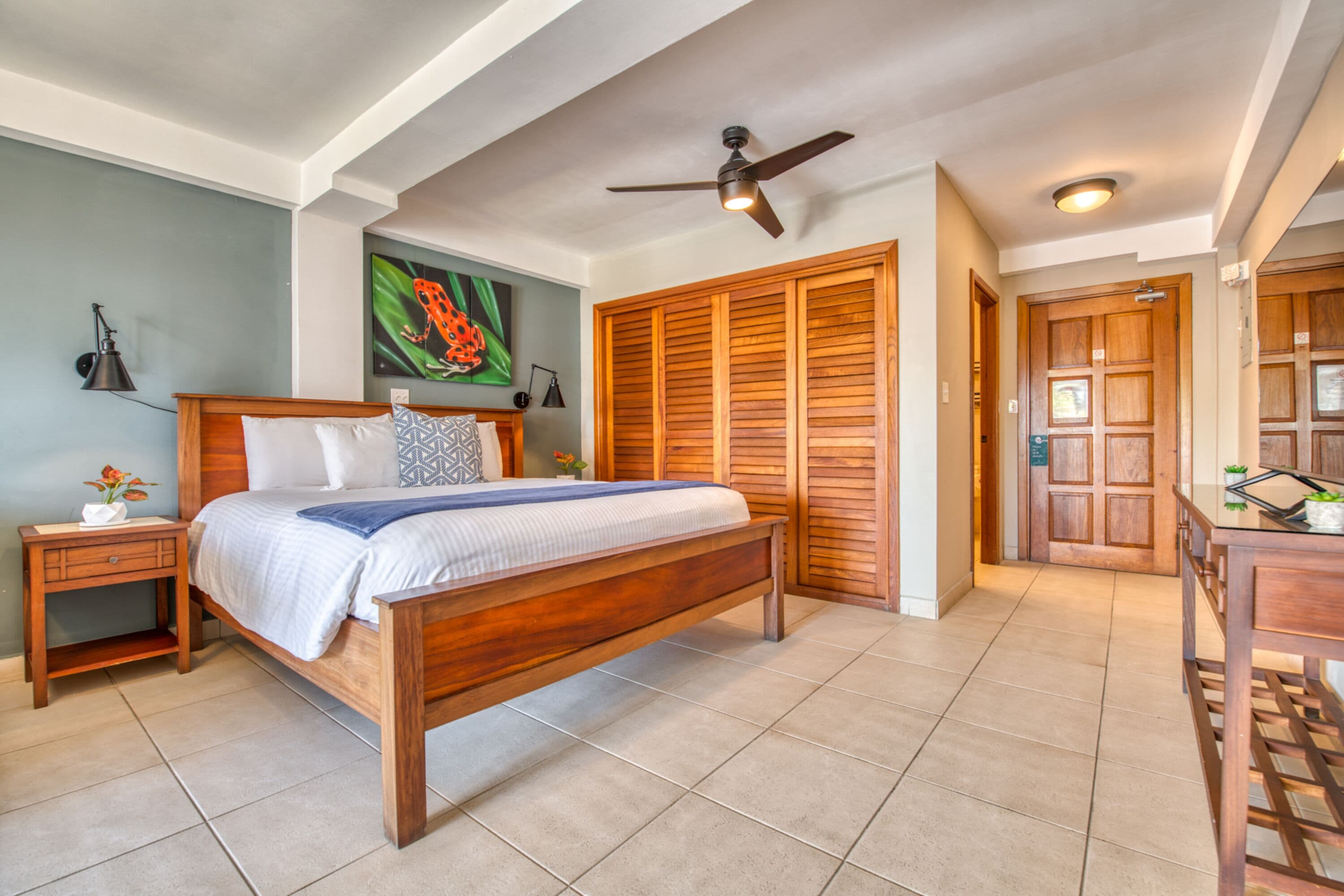 A bedroom with a wooden bed, a nightstand, a ceiling fan, and a large wooden door.