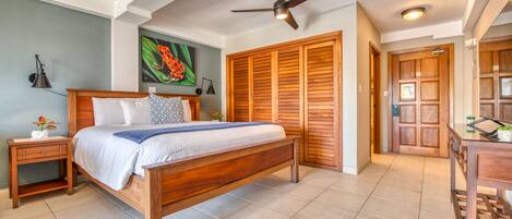 A bedroom with a wooden bed, a nightstand, a ceiling fan, and a large wooden door.