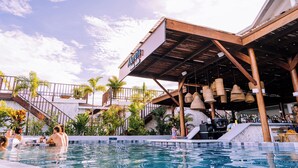 A pool area with a bar and outdoor seating, surrounded by palm trees and a wooden structure with a sign. - Tropical Suites Hotel (Bocas del Toro)