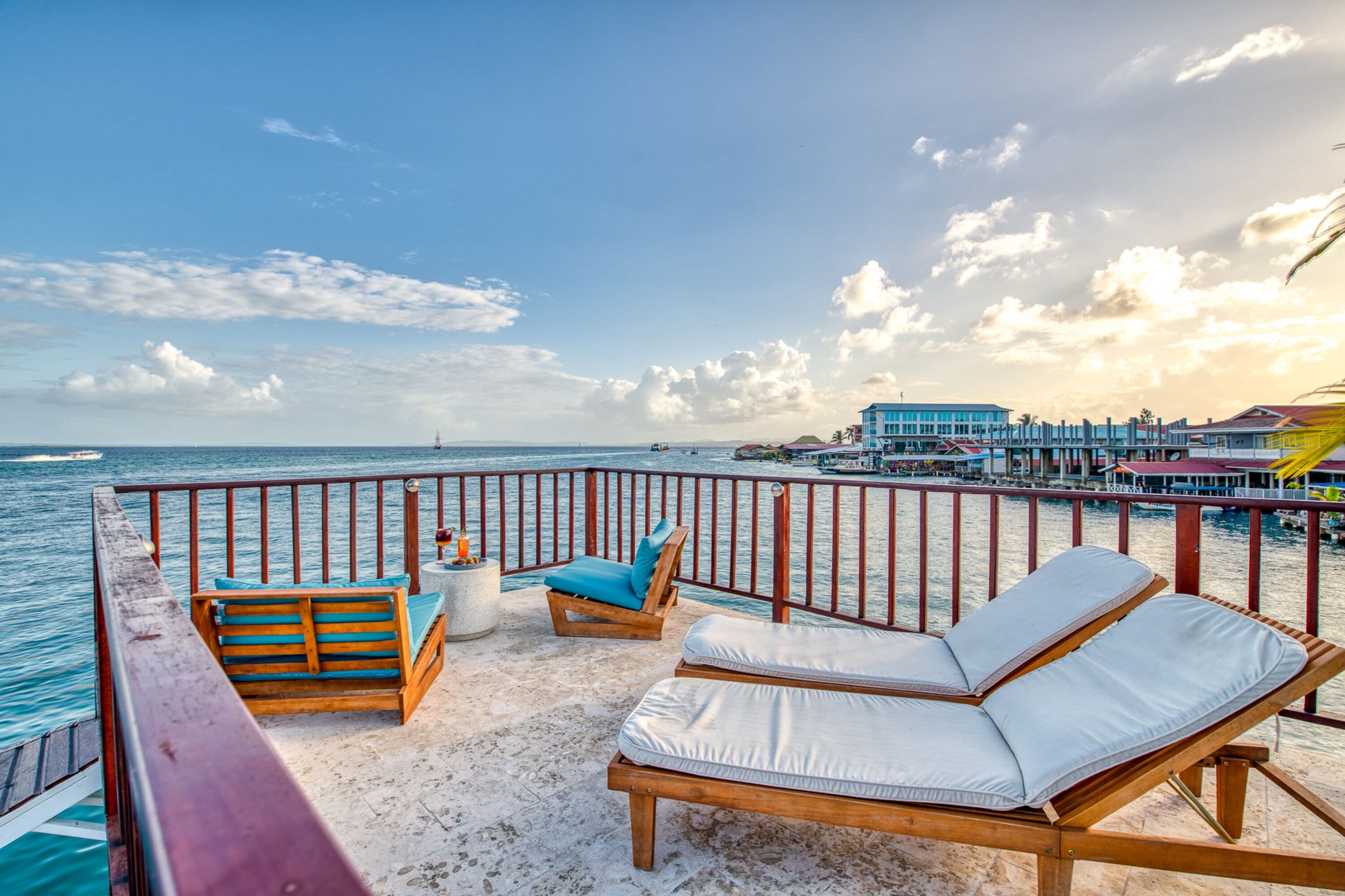 A deck with wooden lounge chairs and a small table, overlooking a beach and ocean.