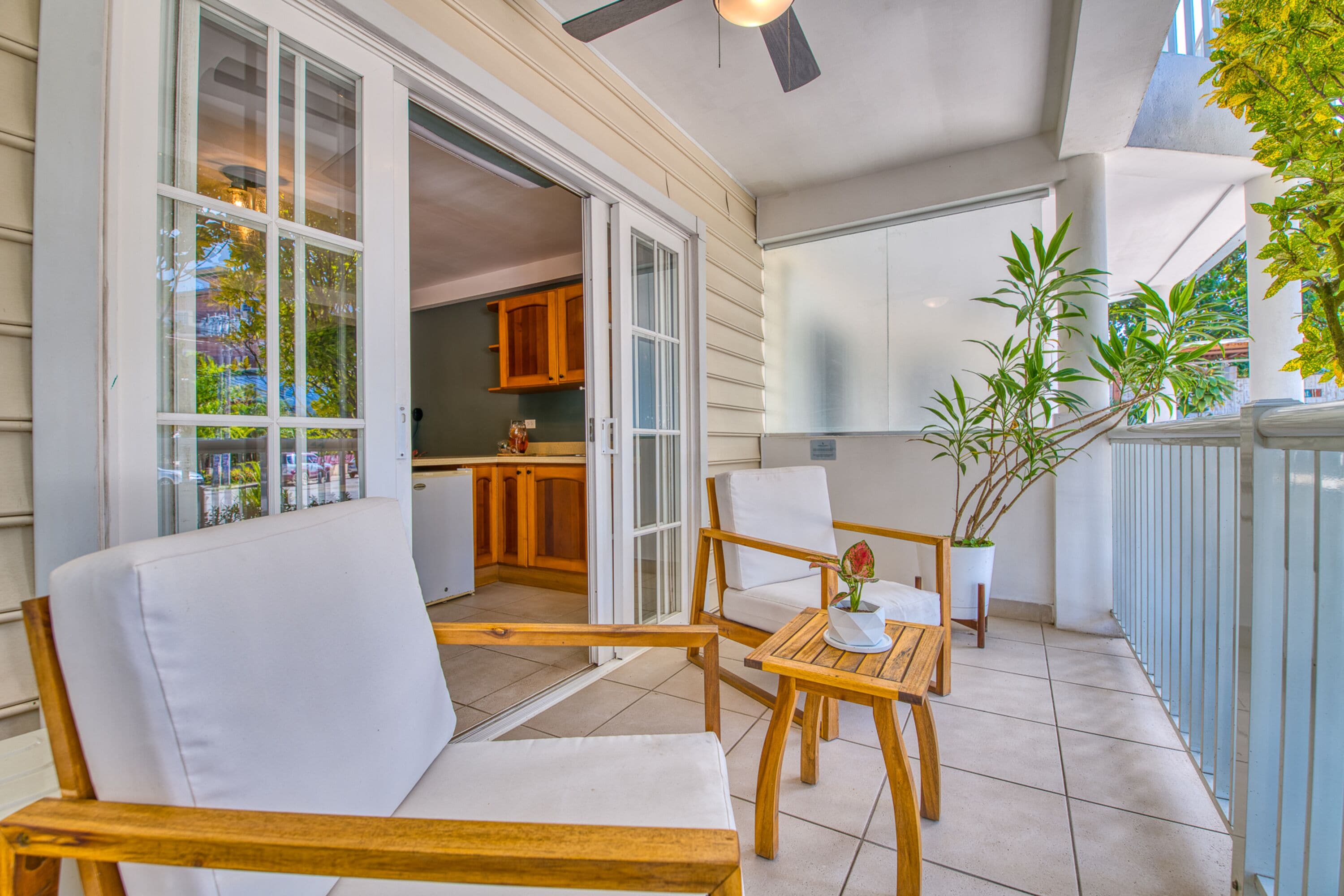 Een balkon met houten meubels, een bloempot en uitzicht op de keuken.