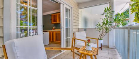 A balcony with wooden furniture, a potted plant, and a view of the kitchen.