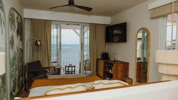 Habitación de hotel con cama, televisión, balcón con vista al mar y un espejo grande.