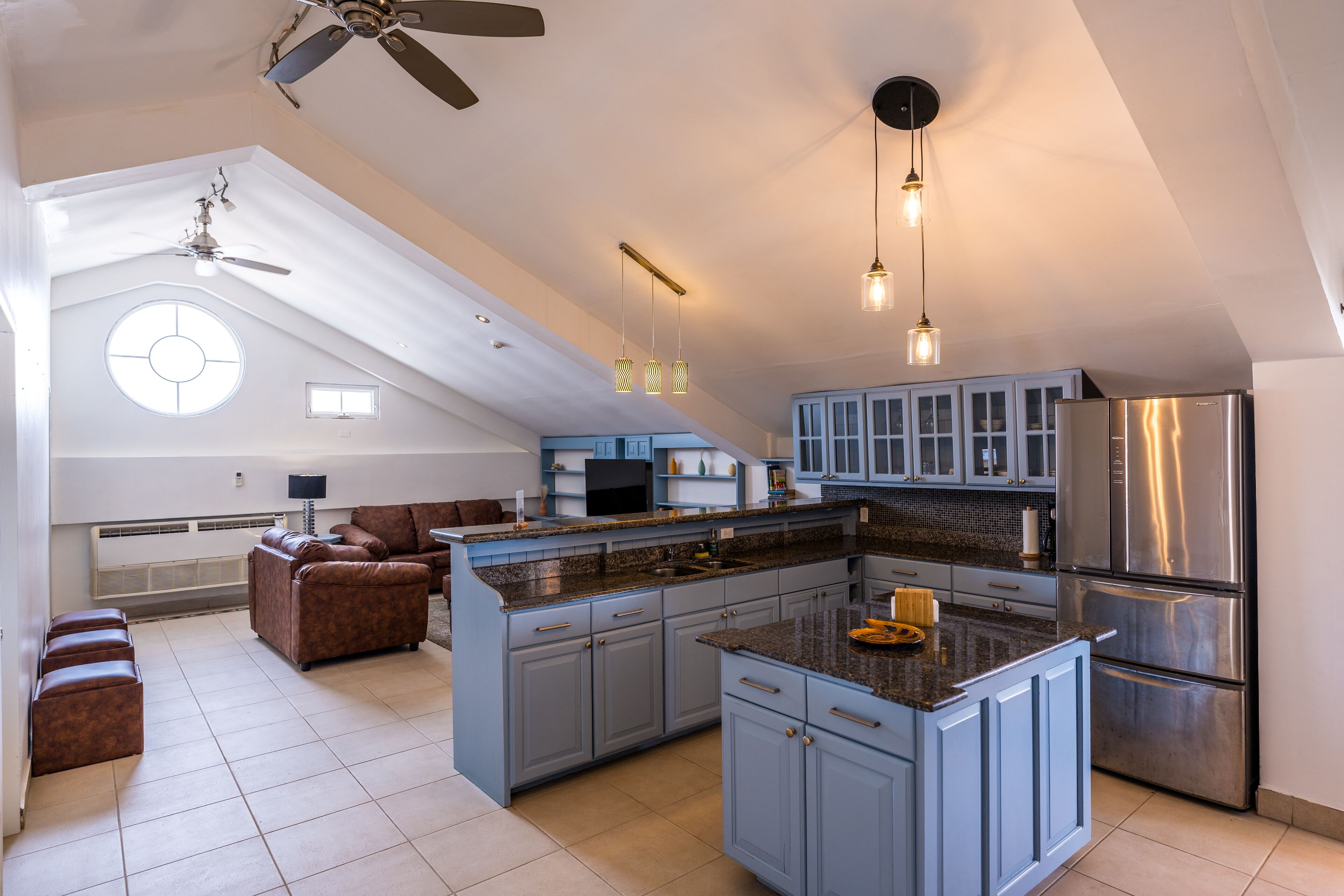 A spacious kitchen with a large island, blue cabinets, and a stainless steel refrigerator.